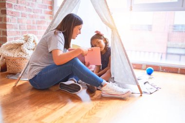 Anaokulunda Tip 'in içinde yerde oturan küçük kıza kitap okuyan güzel bir öğretmen.