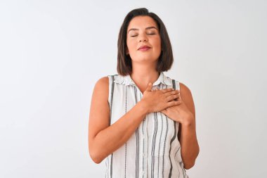 İzole edilmiş beyaz arka plan üzerinde sıradan çizgili tişört giyen genç ve güzel bir kadın. Elleri göğsünde, gözleri kapalı ve yüzünde minnet dolu bir jest ile gülümsüyor. Sağlık kavramı.