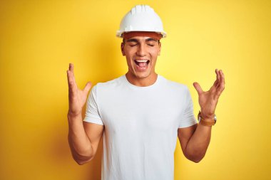 Sarı arka plan üzerinde inşaat kaskı takan yakışıklı genç adam kollarını kaldırmış ve gözlerini kapatmış heyecanla haykırarak başarının çılgınlığını kutluyor. Kazanan konsept