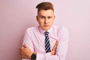 Gömlek ve kravat takan yakışıklı genç bir işadamı. İzole edilmiş pembe arka planda dikiliyor. Kış soğuğu için titriyor ve donuyor.