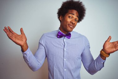 İzole edilmiş beyaz arka plan üzerinde çizgili gömlek ve mor papyon takan afro iş adamı. Kolları ve elleri havada, kafası karışmış bir ifade. Şüphe kavramı.