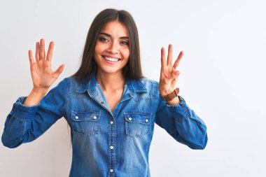 İzole edilmiş beyaz arka plan üzerinde duran sıradan bir kot gömlek giyen genç ve güzel bir kadın 8 numaralı parmaklarıyla işaret ederken kendinden emin ve mutlu bir şekilde gülümsüyor..
