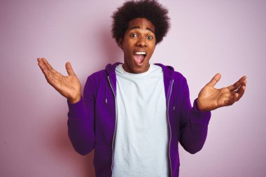 Mor eşofman üstü giyen genç Afro-Amerikan bir adam izole edilmiş pembe arka planda durmuş çılgın ve başarıyı kutlarken kollarını kaldırmış ve gözleri açık bir şekilde heyecanla haykırıyordu. Kazanan konsept