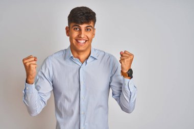 Genç Hintli iş adamı zarif bir gömlek giyerek izole edilmiş beyaz arka planda duruyor. Şaşırmış ve şaşırmış bir şekilde kollarını kaldırıp, gözlerini açarak başarıyı kutluyorlar. Kazanan konsept.