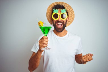 Yazın komik giyinen Hintli adam, izole edilmiş beyaz arka planda kokteyl içerken gururla bağırıyor, zaferi ve başarıyı kutluyor.