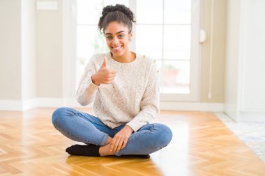 Hareketi el ile mutlu Yaşasın yapıyor katta oturan afro saçlı güzel genç Afro-Amerikan kadın. Kameraya bakarak başarı gösteren ile ifade onaylama.