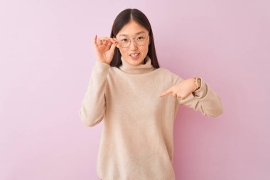 Balıkçı yaka kazak ve gözlük giyen genç Çinli bir kadın izole edilmiş pembe arka planda kendini işaret eden sürpriz bir yüzle.