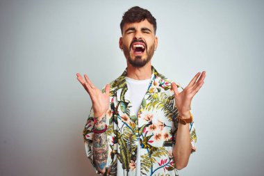 Tatilde dövmeli bir adam, izole edilmiş beyaz arka plan üzerinde durmuş kollarını kaldırmış ve gözlerini kapatmış heyecanlı çığlıklar atarak başarının çılgınlığını kutluyor. Kazanan konsept