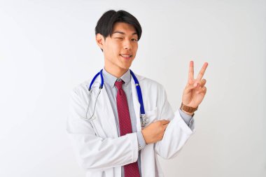 Ceket kravatı takan Çinli doktor ve steteskop ile izole edilmiş beyaz arka plan üzerinde mutlu bir gülümsemeyle kameraya zafer işareti yapıyor. İki numara..