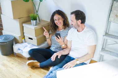 Orta yaşlı çift akıllı telefon kullanarak yeni bir eve taşınıyor. Elleri ve parmakları kenarda mutlu mesut işaret ediyorlar.