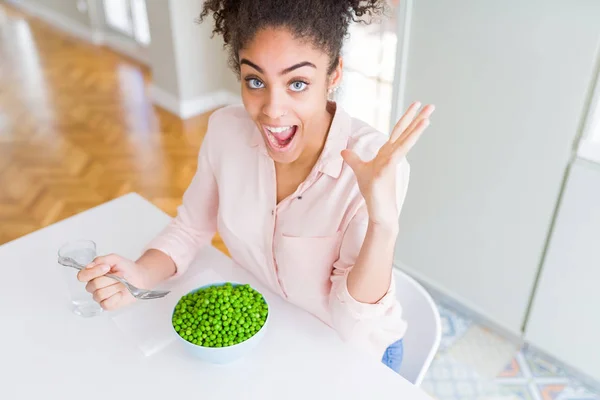 Young african american girl eating healthy green peas very happy and excited, winner expression celebrating victory screaming with big smile and raised hands