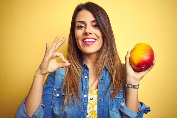 若いです美しい女性食べる新鮮な健康的なマンゴー以上黄色の背景を行いますOk Signとともに指 優れたシンボル — ストック写真