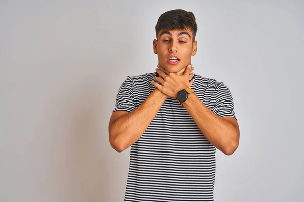 Young indian man wearing navy striped t-shirt standing over isolated white background shouting and suffocate because painful strangle. Health problem. Asphyxiate and suicide concept.