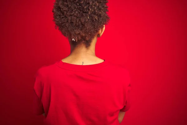 年轻美丽的非洲裔美国女人 有着非洲式的头发 有着孤立的红色背景 背向后站着 双手交叉地将目光移开 — 图库照片