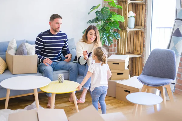 Güzel aile, anne-babalar kanepede kahve içme oturmuş karton kutular etrafında yeni evde oynayan çocuğuna bakıyor