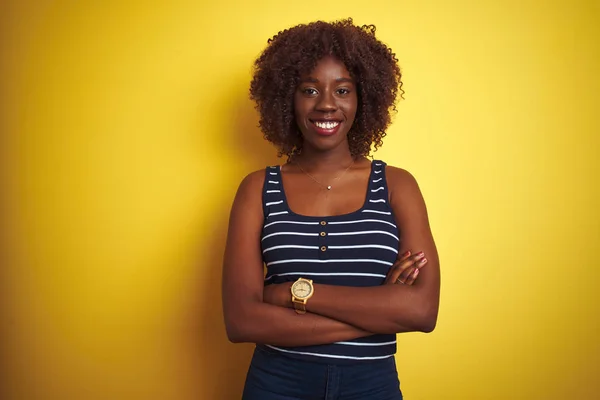 Young african afro woman wearing striped t-shirt over isolated yellow background happy face smiling with crossed arms looking at the camera. Positive person.