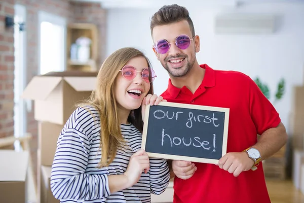 年轻的疯狂的夫妇戴着有趣的眼镜 拿着黑板与我们的第一个家庭文本 高兴和兴奋搬到新的公寓 — 图库照片