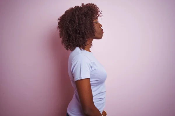 Young african afro woman wearing t-shirt standing over isolated pink background looking to side, relax profile pose with natural face with confident smile.