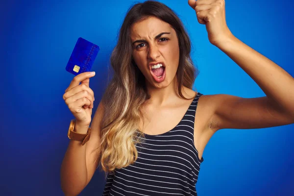 Młoda Piękna Kobieta Trzyma Kartę Kredytową Nad Niebieskim Odosobnionym Tle — Zdjęcie stockowe