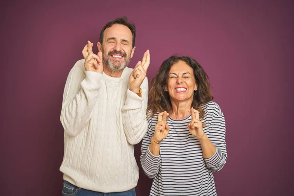 아름답고 중년의 부부가 스웨터 보라색 배경에 손가락을 흔들며 미소를 미신적 — 스톡 사진