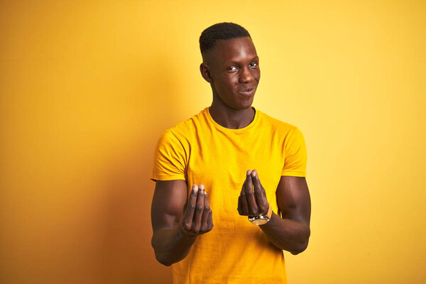 Young african american man wearing casual t-shirt standing over isolated yellow background doing money gesture with hands, asking for salary payment, millionaire business
