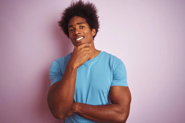 黑头发的非裔美国人穿着蓝色T恤 站在孤立的粉色背景上 微笑着看着相机 双手交叉 下巴向上举起 积极地思考 — 图库照片