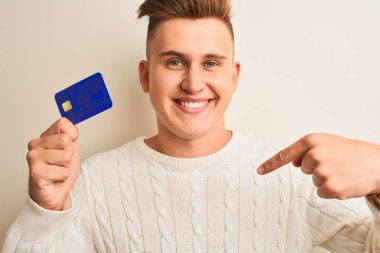 Genç ve yakışıklı bir adam kredi kartını soyutlanmış beyaz arka planda tutuyor.