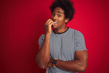 Afro saçlı genç Amerikalı adam izole edilmiş kırmızı arka plan üzerinde denizci çizgili tişört giyiyor. Ağzı tırnak yiyen elleri yüzünden gergin ve stresli görünüyor. Endişe sorunu.