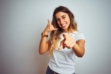 İzole edilmiş arka planda günlük beyaz tişört giyen genç ve güzel bir kadın gülümsüyor telefonda konuşarak seni işaret ediyor. Ara beni..