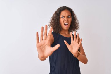 İzole edilmiş beyaz arka plan üzerinde duran mavi elbiseli genç Brezilyalı kadın korku ifadesinden korkuyor ve dehşete düşüyor. El hareketlerini durdur, şok içinde bağır. Panik konsepti.