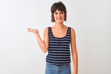 İzole edilmiş beyaz arka plan üzerinde duran çizgili tişört giyen genç ve güzel bir kadın neşeli bir şekilde gülümseyerek kameraya bakıyor..