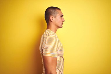 Sarı izole arka planda yan arıyor üzerinde çizgili t-shirt giyen genç yakışıklı adam, güvenli bir gülümseme ile doğal yüzü ile profil poz rahatlayın.