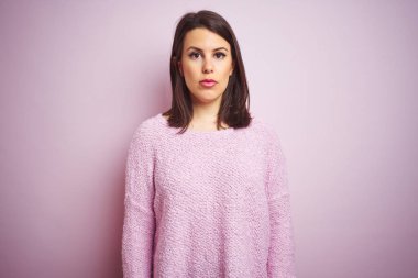 Pembe izole arka plan üzerine kazak giyen güzel esmer kadın yüzünde ciddi bir ifadeyle rahatlamış. Basit ve doğal bir şekilde kameraya bakıyorsun..
