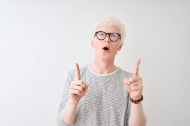 İzole edilmiş beyaz arka plan üzerinde çizgili tişört ve gözlük takan genç albino sarışın adam şaşkın şaşkın yukarı bakıp parmaklarıyla işaret ediyor ve kollarını kaldırıyordu..