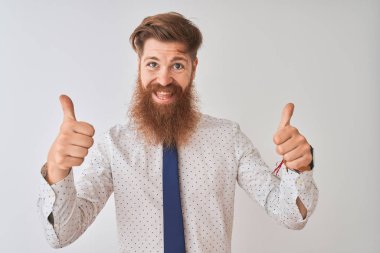 Genç kızıl saçlı İrlandalı işadamı, izole edilmiş beyaz arka plan başarısı tabelasının üzerinde duruyor. Elleriyle olumlu bir jest yapıyor, gülümsüyor ve mutlu. Neşeli ifade ve kazanan jest.