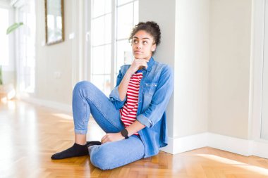 Çene düşünme hakkında soru, dalgın ifade üzerine el ile katta oturan afro saçlı güzel genç Afro-Amerikan kadın. Düşünceli yüzüyle gülümsüyor. Şüphe kavramı.