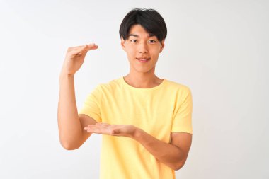 Sarı günlük tişört giyen Çinli bir adam izole edilmiş beyaz arka plan üzerinde duruyor. Elleri büyük ve büyük boy işareti, ölçü sembolü gösteriyor. Kameraya bakıp gülümsüyor. Ölçüm konsepti.