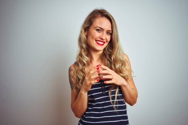 İzole edilmiş beyaz arka plan üzerinde duran çizgili tişört giyen genç ve güzel bir kadın ellerini birleştirip gülümseyerek gevşemiş ve neşeli olmasını diliyordu. Başarı ve iyimser