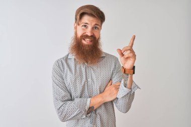 Yüzünde büyük bir gülümseme ile izole beyaz arka plan üzerinde ayakta rahat gömlek giyen genç Redhead İrlandalı adam, kamera bakarak yan el ve parmak ile işaret.