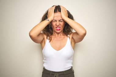 Orta yaş yaşlı kadın beyaz izole arka plan üzerinde baş ağrısı umutsuz muzdarip ayakta ve stresli çünkü ağrı ve migren. Eller baş üstünde.