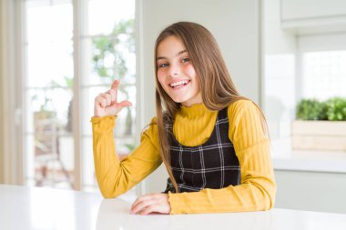 Genç, güzel sarışın kız evde sarı süveter giyiyor gülümsüyor ve kendinden emin el hareketleriyle küçük beden işareti yapıyor parmaklarıyla bakıyor ve kameraya bakıyor. Ölçü kavramı.