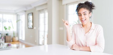 Afro saçlı, yüzünde kocaman bir gülümseme olan güzel Afro-Amerikan kadınının geniş açısı, kameraya el ile işaret ediyor..