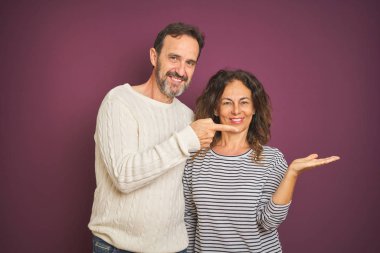 Güzel orta yaşlı çift, izole edilmiş mor arka plan üzerine kış süveteri giyip kameraya hayret ediyor ve gülümsüyor..