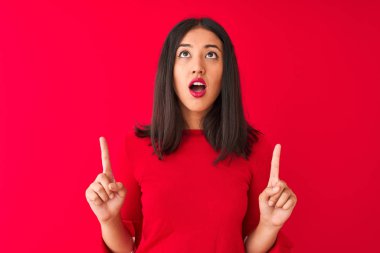 Genç, güzel Çinli bir kadın, gündelik elbiseler giyip kırmızı arka planda dikilmiş şaşkın şaşkın bakıyor, parmaklarıyla işaret ediyor ve kollarını kaldırıyordu..