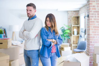 Karton kutuların etrafında duran genç ve güzel bir çift şüpheci ve gergin, kollarını kavuşturmuş yüz ifadesini onaylamıyor. Negatif kişi.