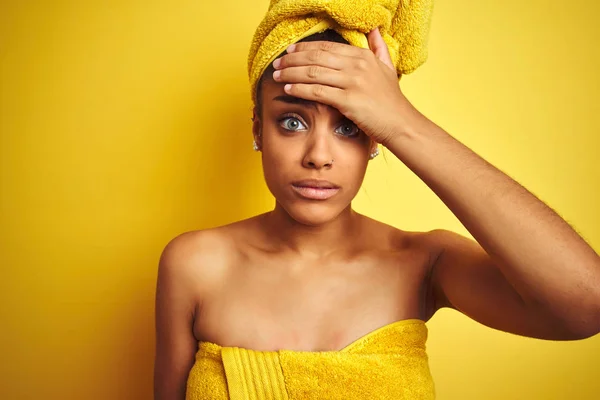 Young african american woman wearing towel after shower over isolated yellow background stressed with hand on head, shocked with shame and surprise face, angry and frustrated. Fear and upset for mistake.