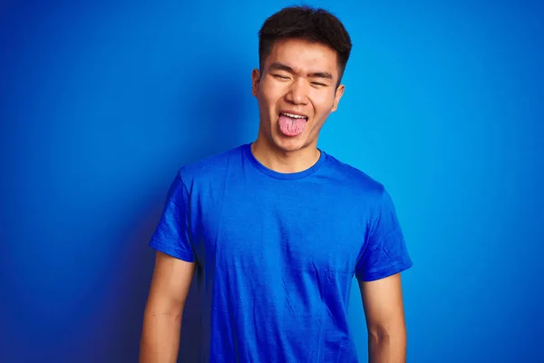 Tシャツを着た若いアジア系中国人男性が独立した青い背景の上に立ち 面白い表情で幸せを舌に突き出している 感情概念 — ストック写真