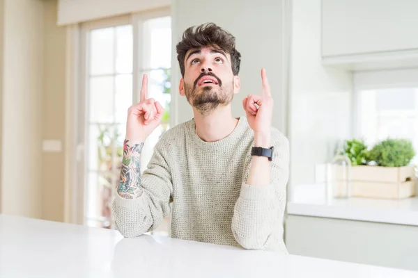 Hombre Joven Con Suéter Casual Sentado Mesa Blanca Asombrado Sorprendido — Foto de Stock