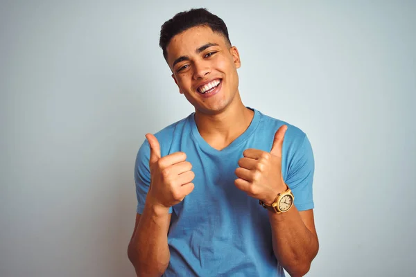 年轻的巴西男人穿着蓝色的T恤 站在孤立的白色背景下 成功的标志着手拿着积极的手势 微笑着竖起大拇指 快乐地 快乐的表情和胜利的姿态 — 图库照片