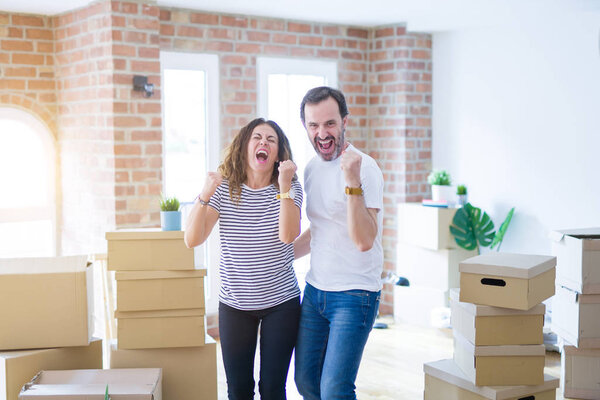 Middle age senior couple moving to a new home with boxes around very happy and excited doing winner gesture with arms raised, smiling and screaming for success. Celebration concept.